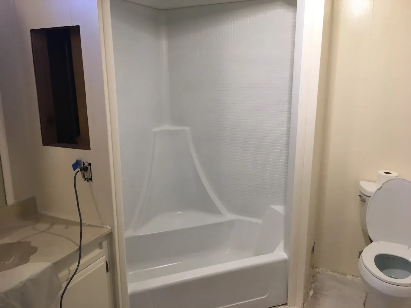 Bathroom with white shower stall, built-in seat, and toilet beside a sink counter