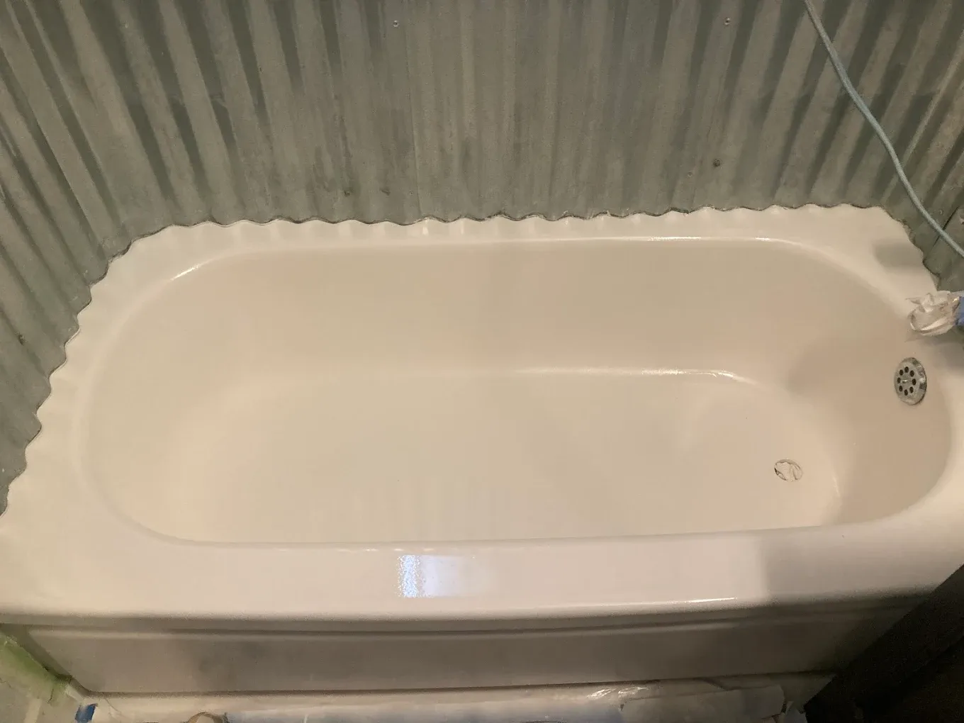 White bathtub with beige surround in a small bathroom, viewed from above.