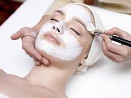 Person receiving facial treatment with a white mask applied, lying down, eyes closed, in a spa setting.