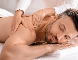 Man receiving a shoulder massage; close-up with eyes closed. White sheet, therapist's hands.