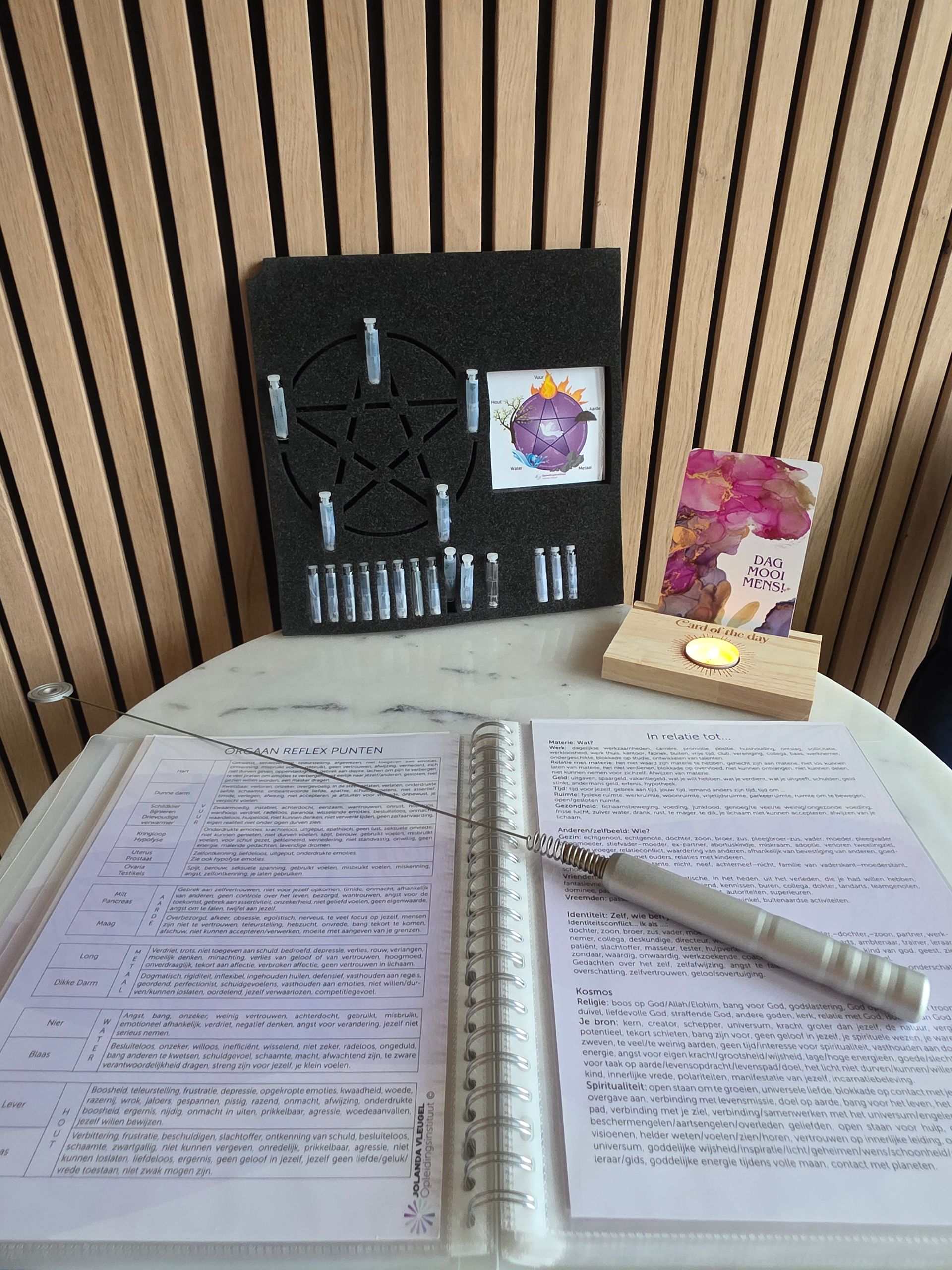 Een tafel met een open boek, pen en versieringen, waaronder een pentagram en een kaarsenhouder met bloemen.