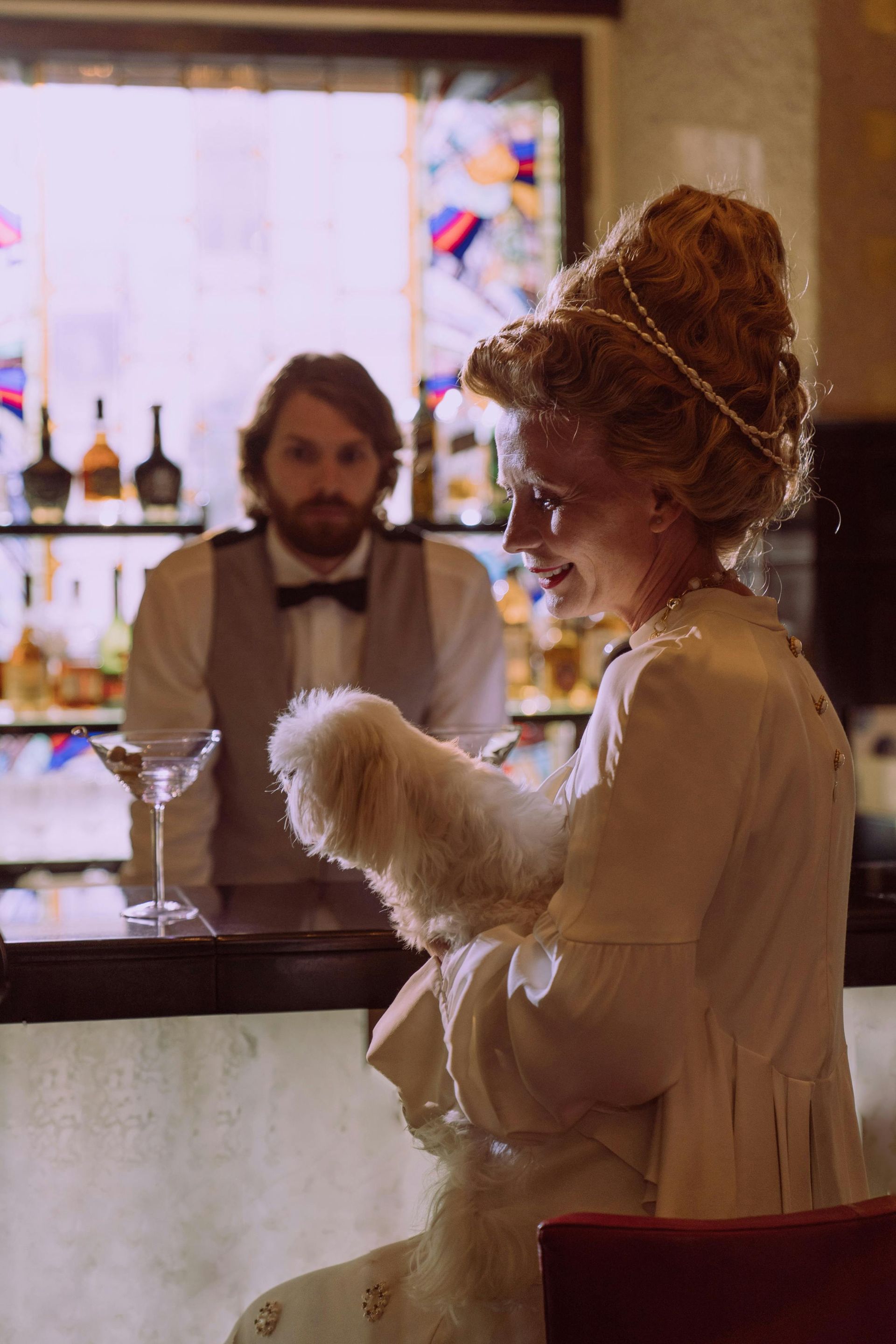 A woman in a white dress is sitting at a bar holding a martini glass.