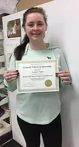 Young woman holding a certificate from a grooming school, smiling, wearing a light teal hoodie.