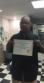 Man in black shirt holding certificate, likely in a barber shop.