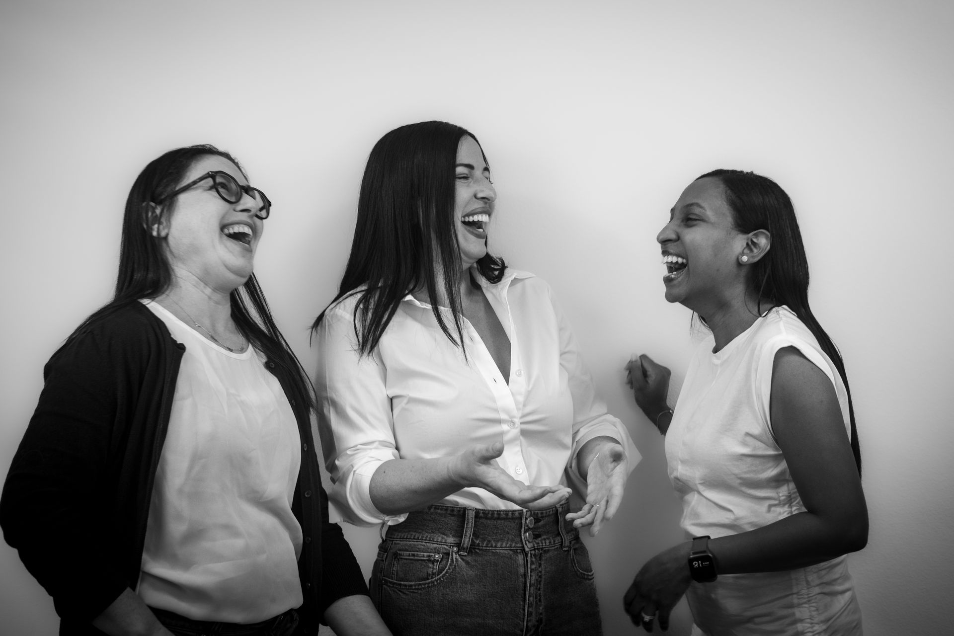 A group of women are standing next to each other and laughing in a black and white photo. A group of women are standing next to each other and laughing in a black and white photo.