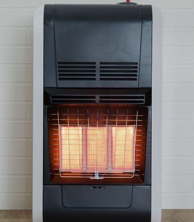 A gas heater is sitting on a wooden floor in front of a white brick wall.