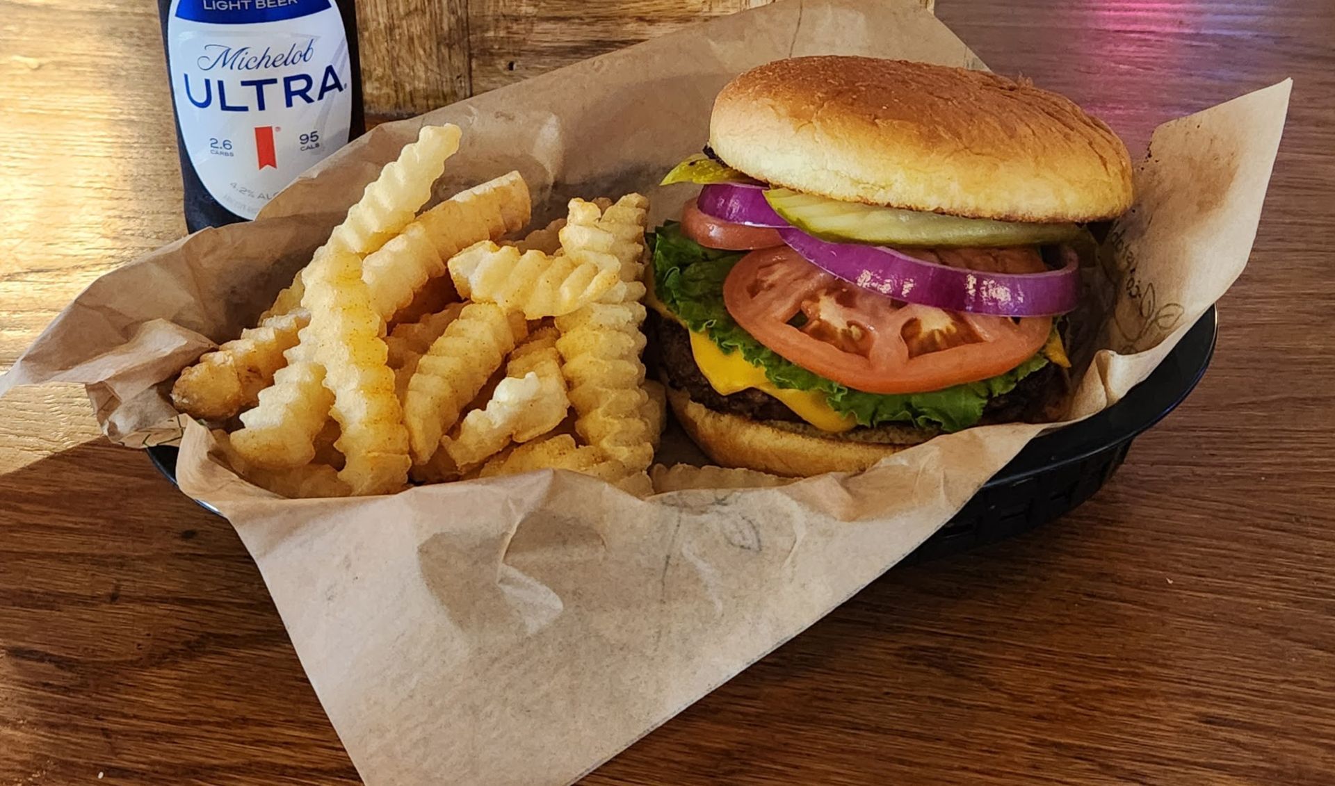 Burger with fries on a tray and a can of Ultra beer on a wooden table