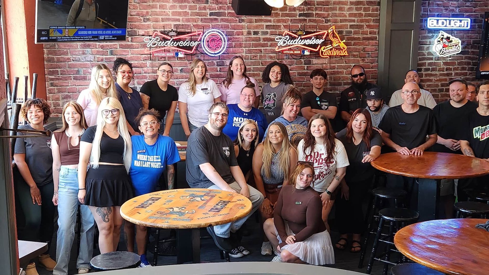 Large group posing in a rustic restaurant, with brick walls, neon signs, and wooden tables.