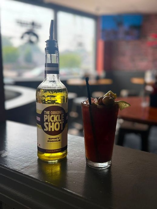 Bottle of yellow peach liqueur beside a dark red cocktail on a bar table.