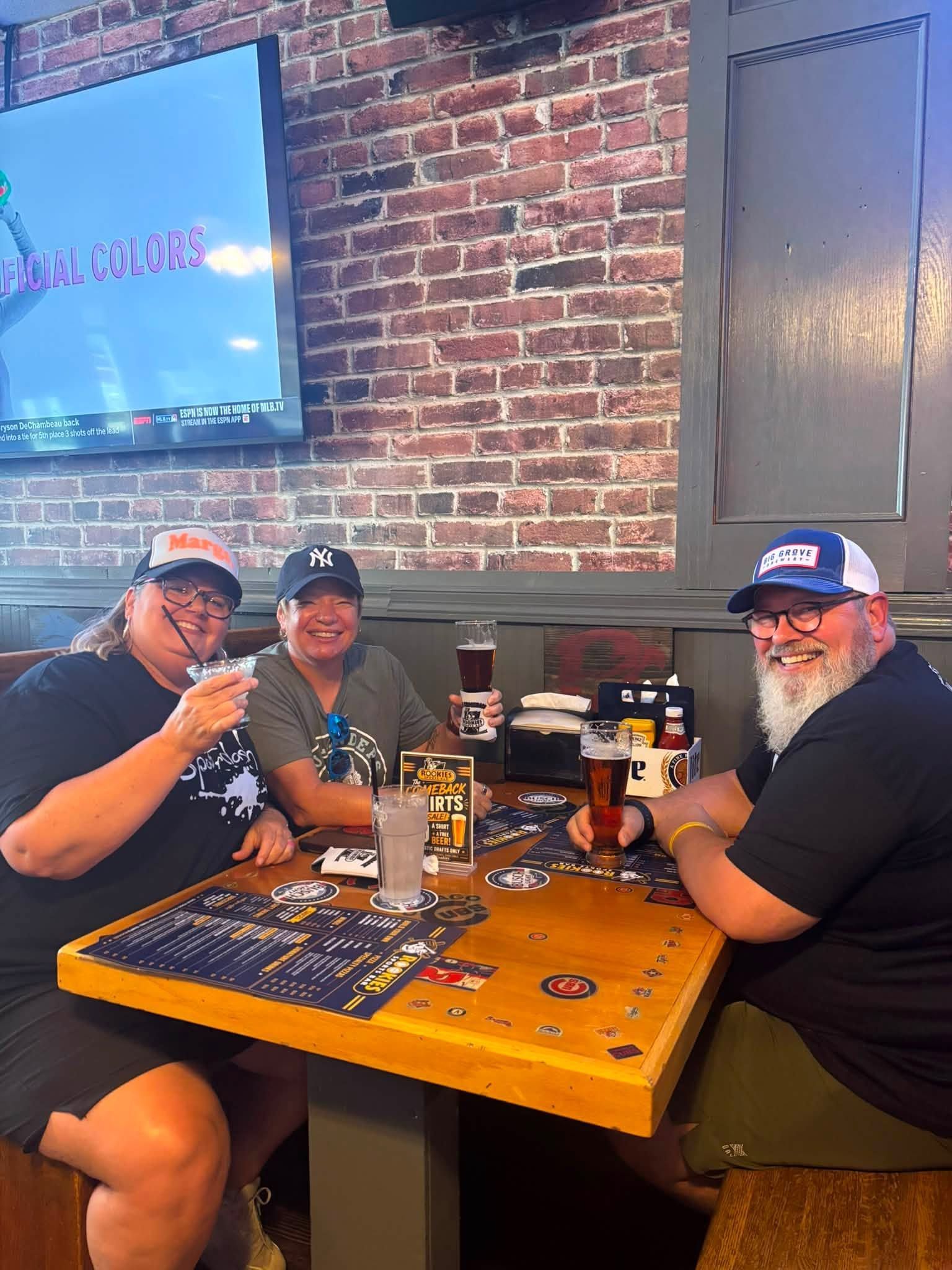 Three people seated at a restaurant table with drinks and board games against a brick wall.