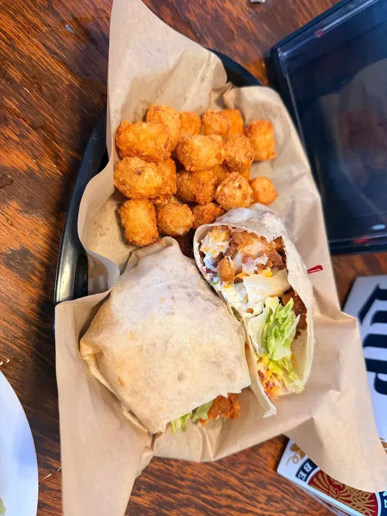 A wrapped sandwich and a pile of golden tater tots on a tray