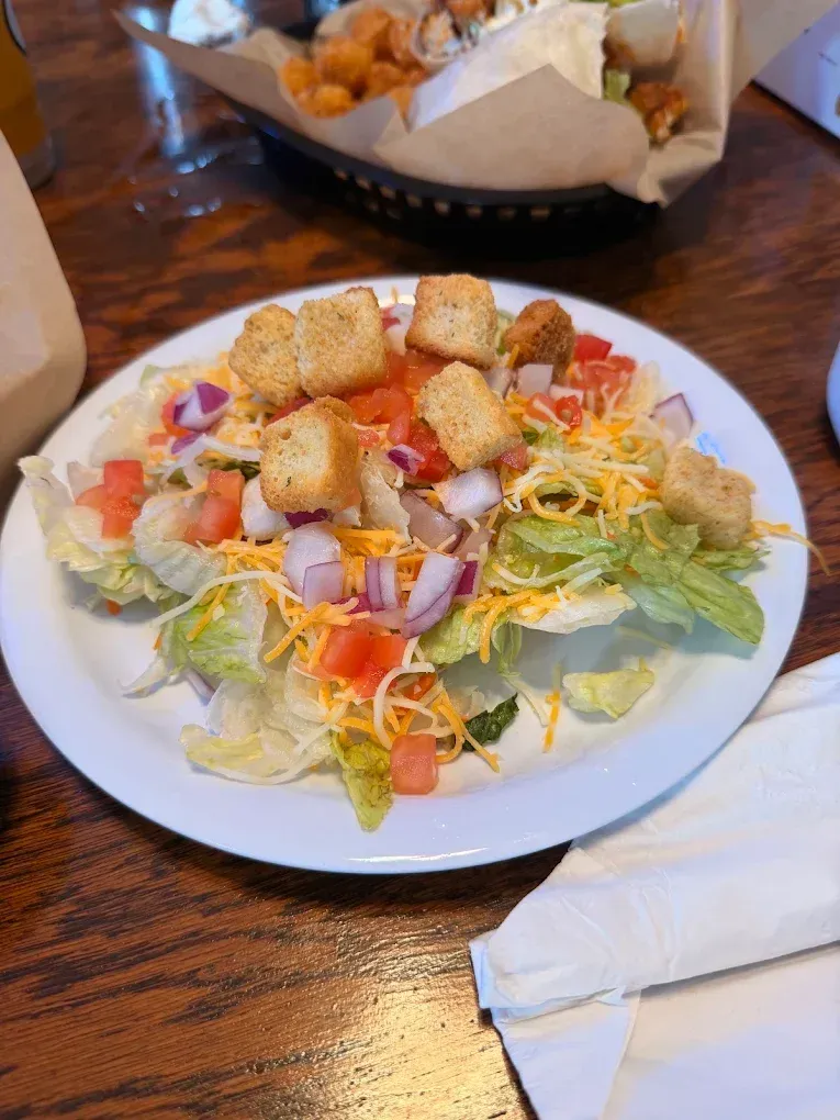 Caesar salad with croutons on a white plate on a wooden table, with a bread basket in the background