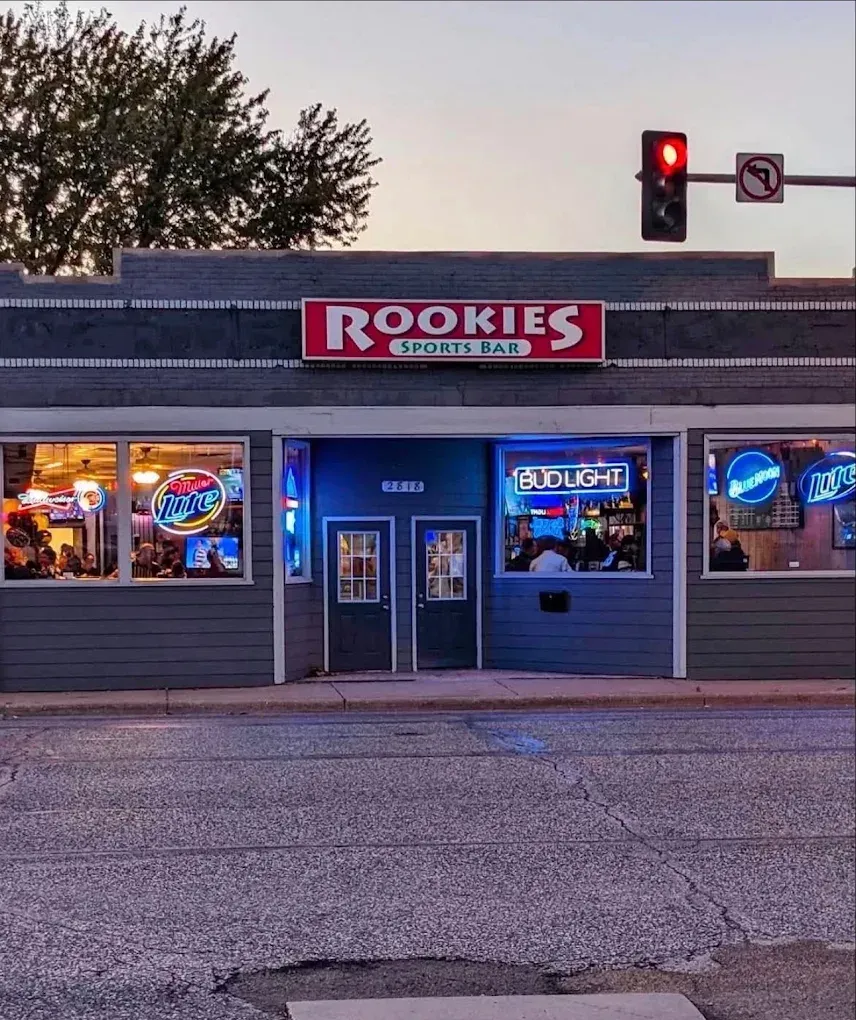 Rookies sports bar storefront at dusk with neon signs and a red traffic light overhead