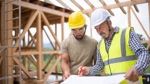Two construction workers in hard hats reviewing plans at a building site