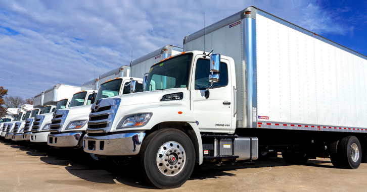 White box trucks lined up in a row at an outdoor lot under a blue sky