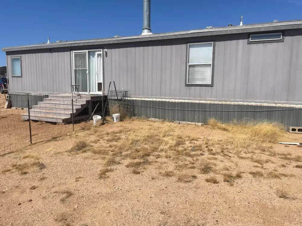Gray mobile home with stairs, door, and a dry, brown yard.