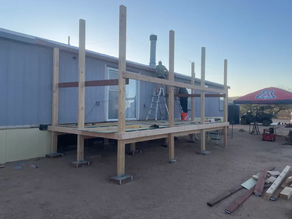 Deck construction in progress; wooden posts and beams being installed on a raised platform next to a building.