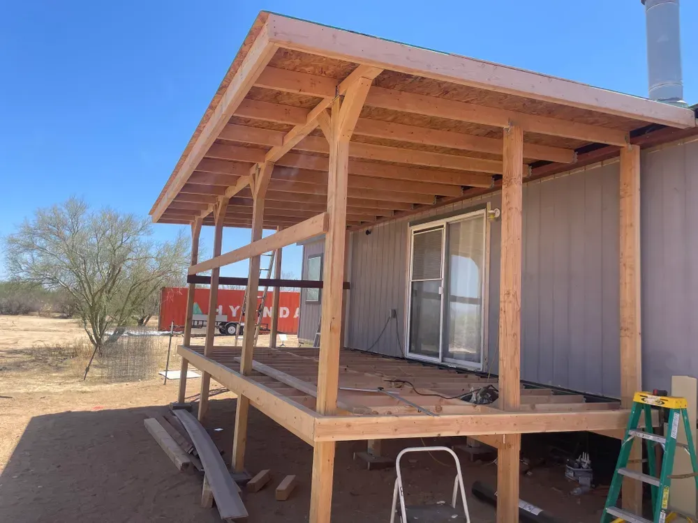 Wooden porch being built with a sliding glass door and metal siding. Blue sky, desert background.