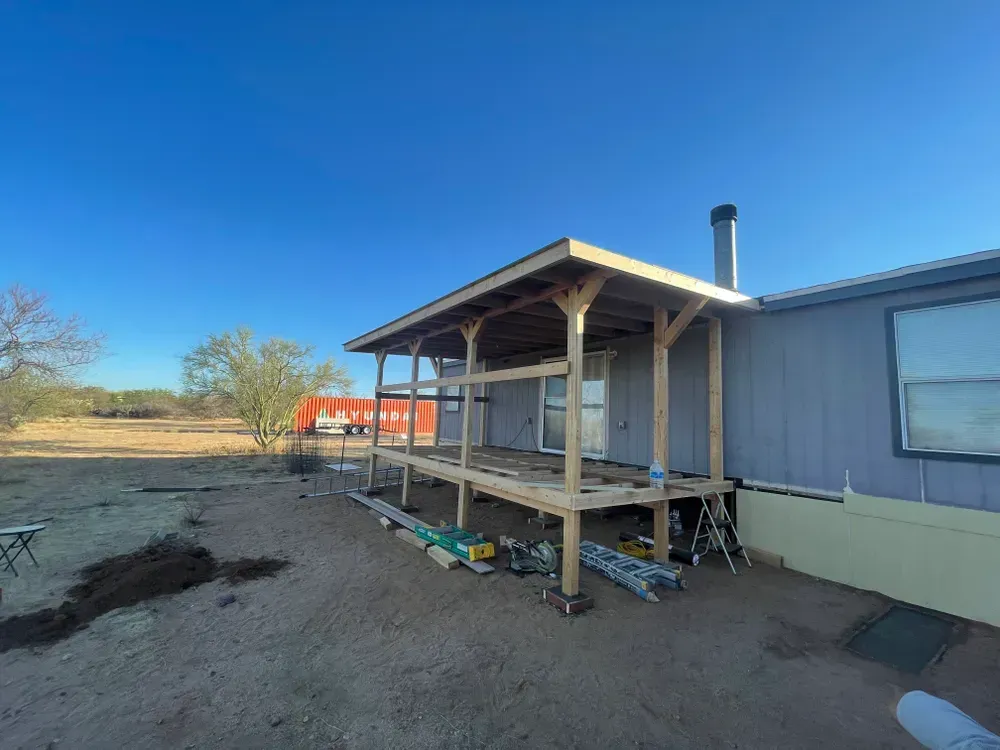Construction of a wooden porch attached to a light blue mobile home; clear sky.