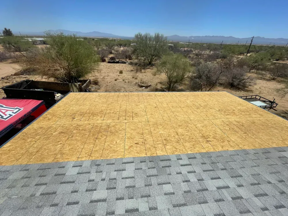 Rooftop view with gray shingles in the foreground, wooden OSB, and desert landscape with blue sky.