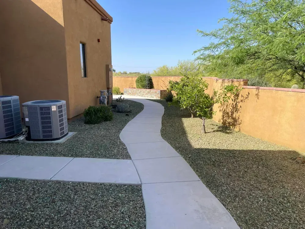 Concrete walkway winds between tan walls and gravel landscaping, under a bright blue sky.