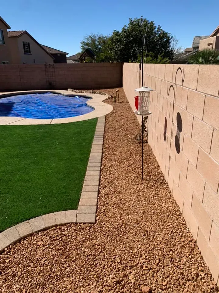 Backyard with pool and artificial turf, bordered by stone and a block wall with bird feeder.