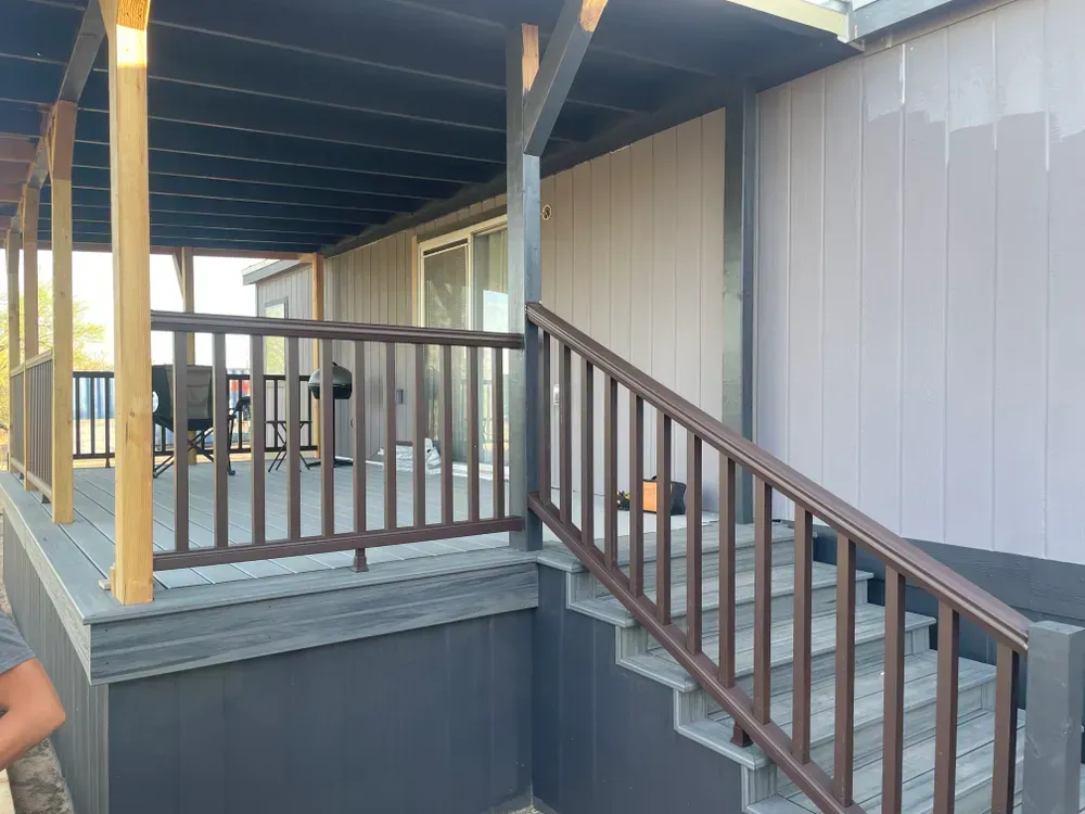 Brown railing leads to a covered porch with a sliding glass door. Gray siding and deck.