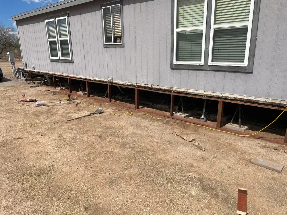 Mobile home with exposed undercarriage undergoing repair in a dirt lot.