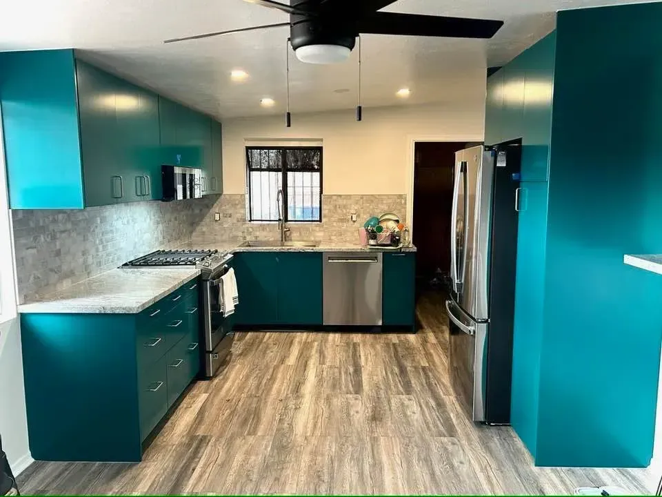 Teal kitchen with cabinets, stainless steel appliances, and gray countertops. Wooden flooring.