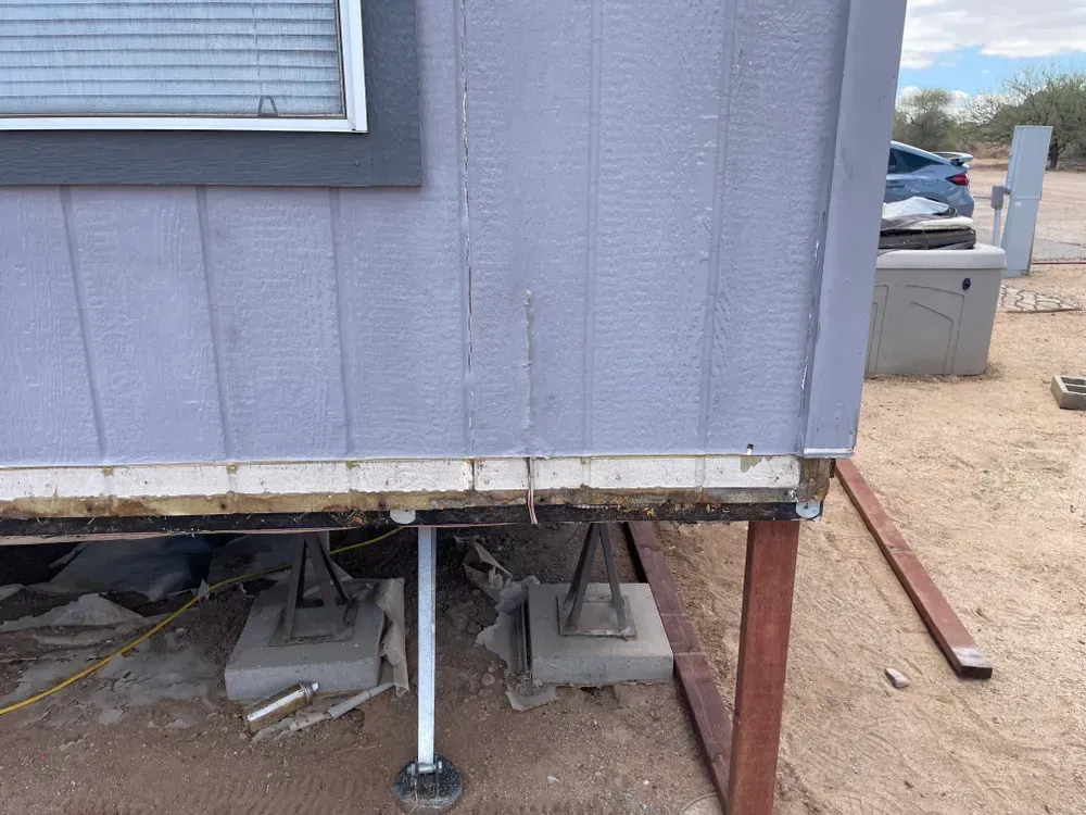 Exterior of a light purple mobile home. Underside of home with support beams visible.