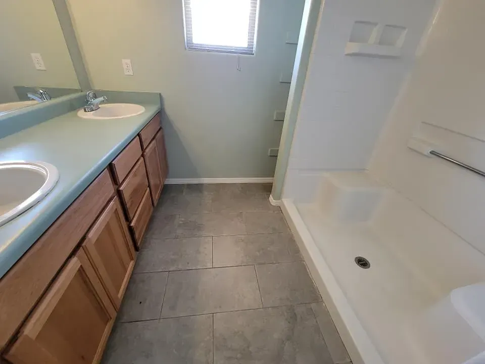 Bathroom with double sinks, light green walls, tile floor, and a white shower.