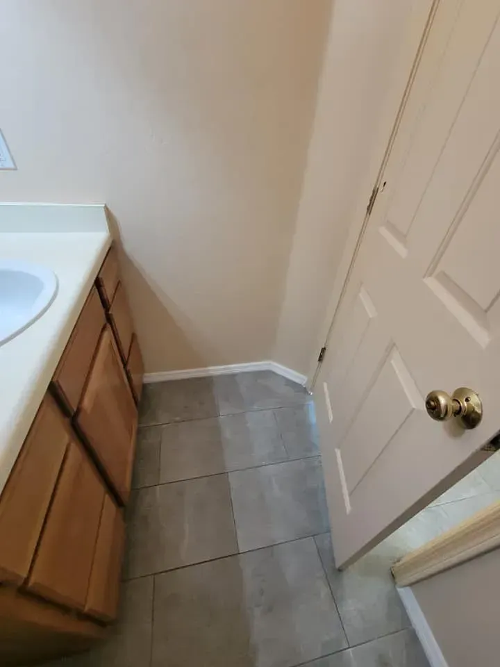 Bathroom with vanity, cabinets, and a door, grey tiled floor, beige walls.