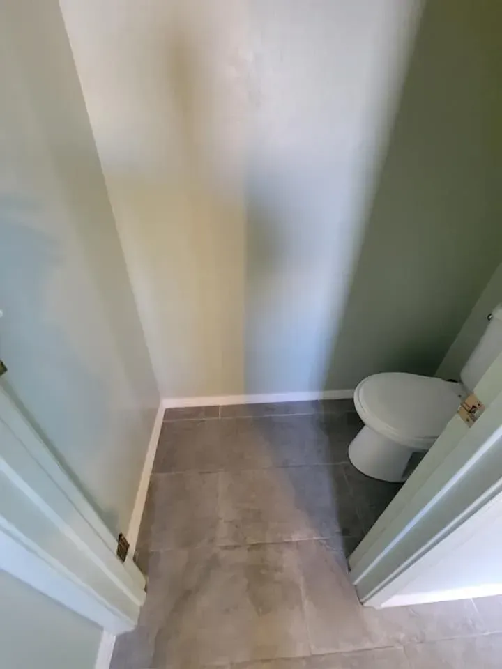 Narrow bathroom with gray tile floor, white toilet, and green and white walls.