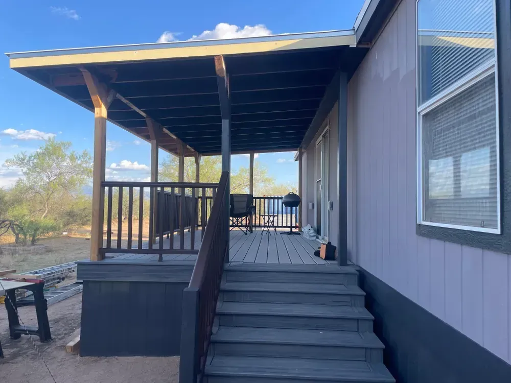 A covered porch with steps leading up to a house with a window, in an outdoor setting.