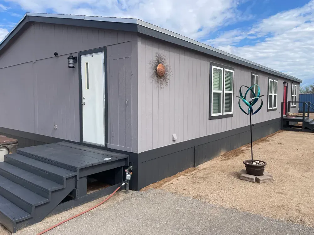 Gray modular building with steps, sun decor, windows, and a blue decorative sculpture.