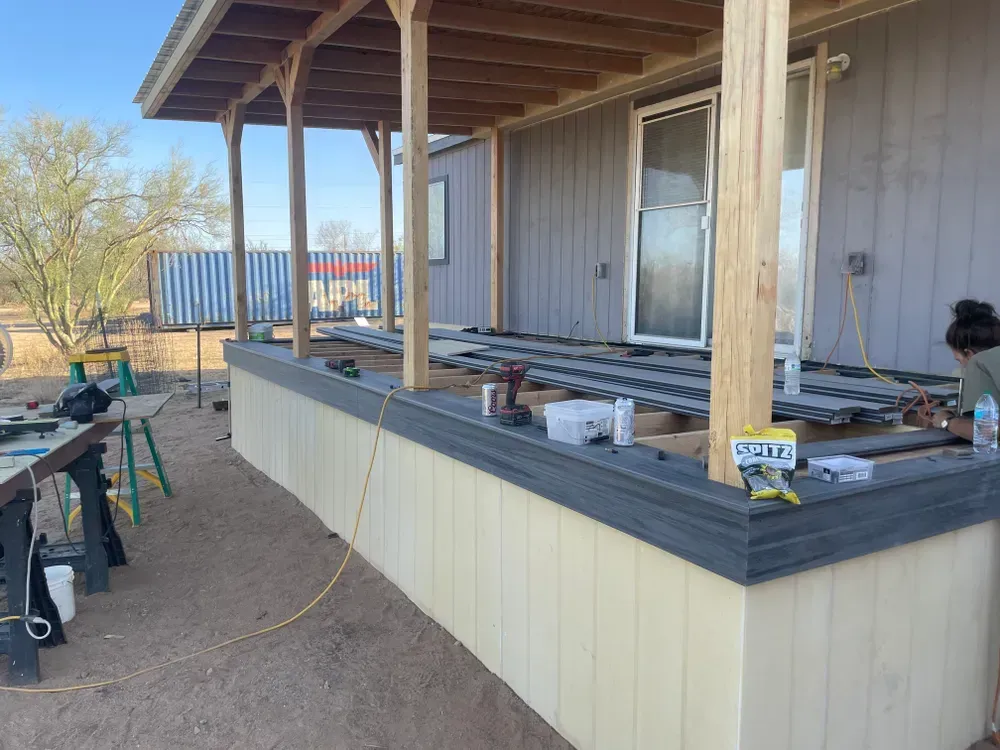 A person works on a new porch with a low skirting and a wooden roof on a house in an outdoor setting.