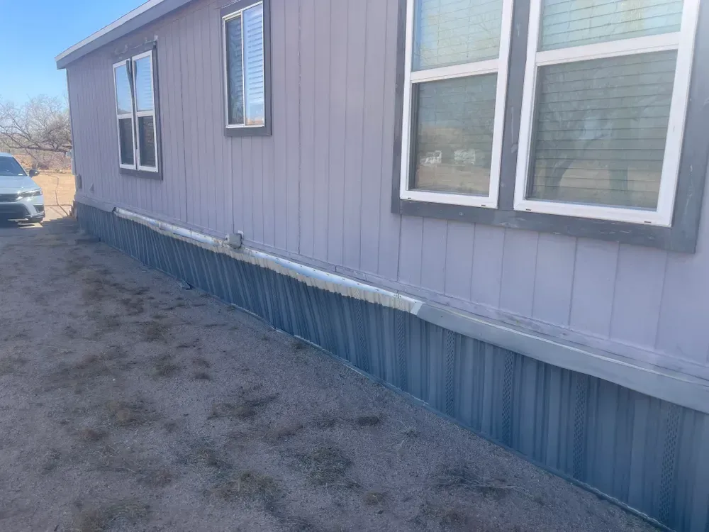 Exterior view of a light purple mobile home with blue siding on a grassy lot.