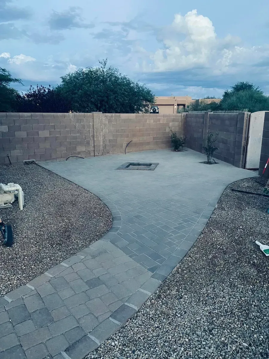 Stone patio enclosed by a cinder block wall, with a small fire pit, and gravel landscaping under cloudy skies.