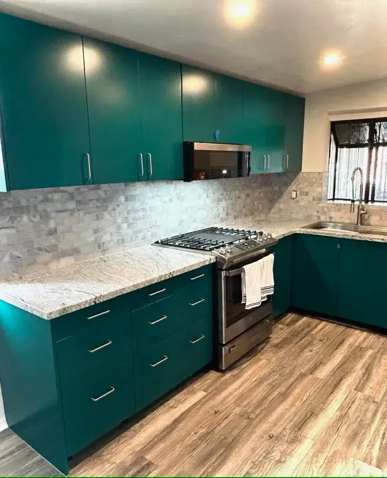 Teal kitchen cabinets, stainless steel appliances, light countertops, and wood-look flooring.