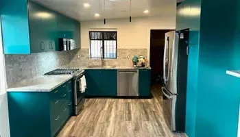 Teal kitchen with stainless steel appliances, light gray countertops, and wood-look flooring.