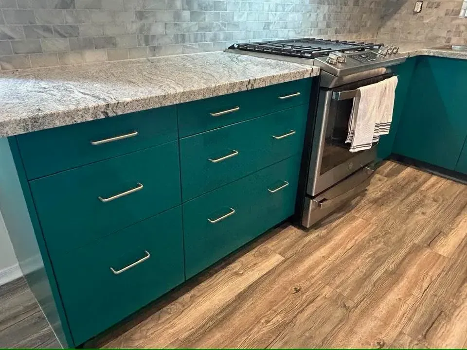 Teal kitchen cabinets with granite countertop, stainless steel oven, and wood-look flooring.