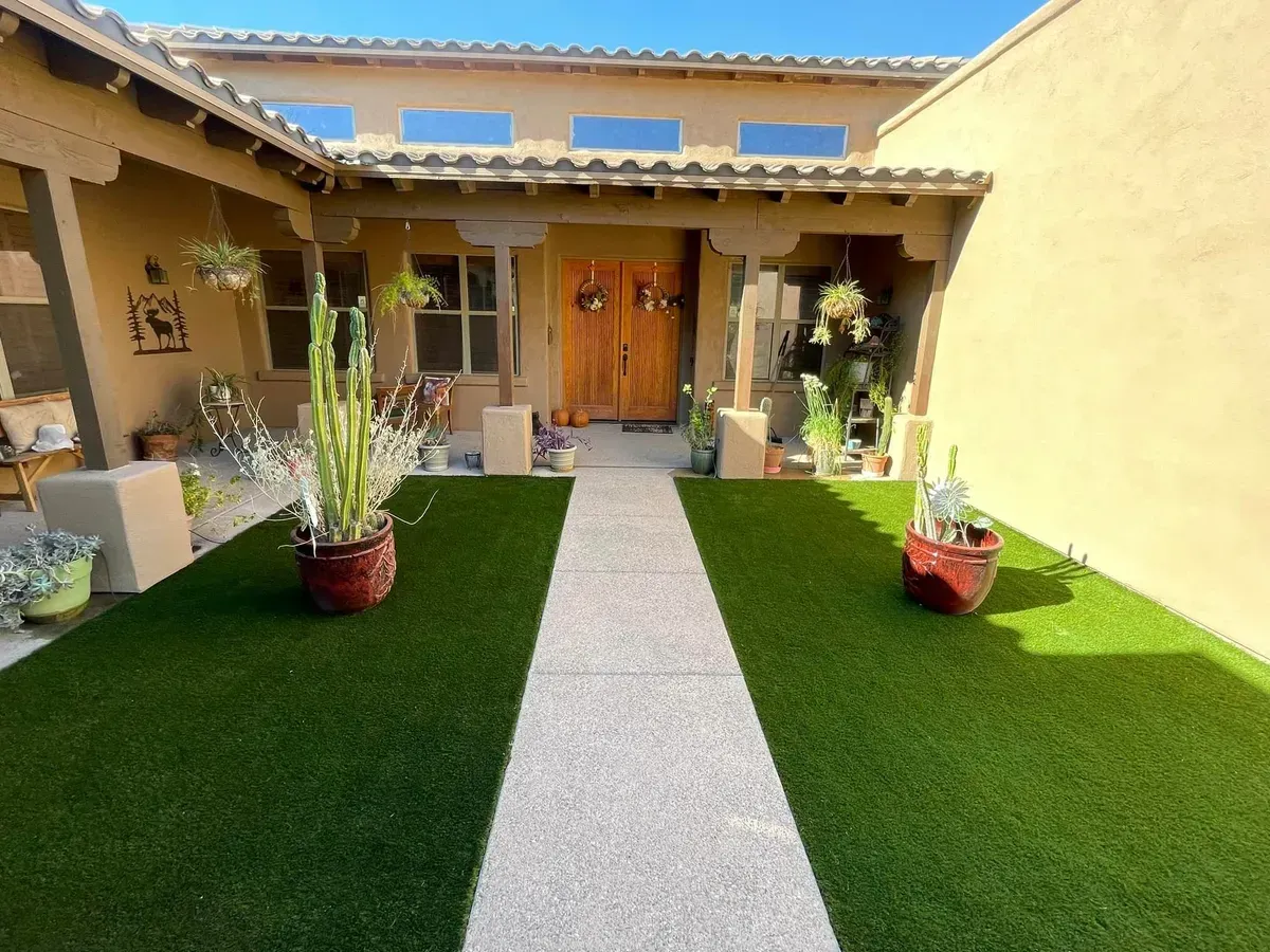 Exterior view of a house with a concrete walkway leading to the front door, flanked by green turf and potted plants.
