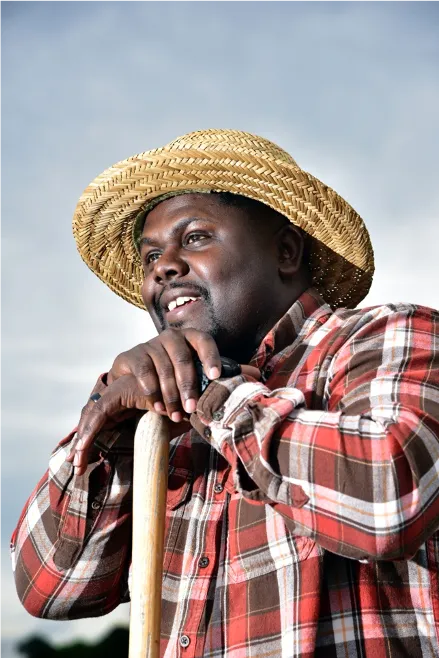 A local farmer smiling in a green field at sunrise