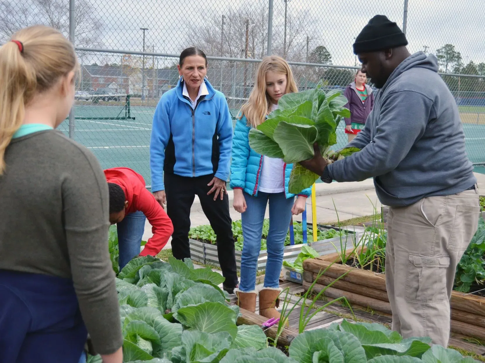 A Flint River Fresh educator shows students a harvested collard head in a school garden