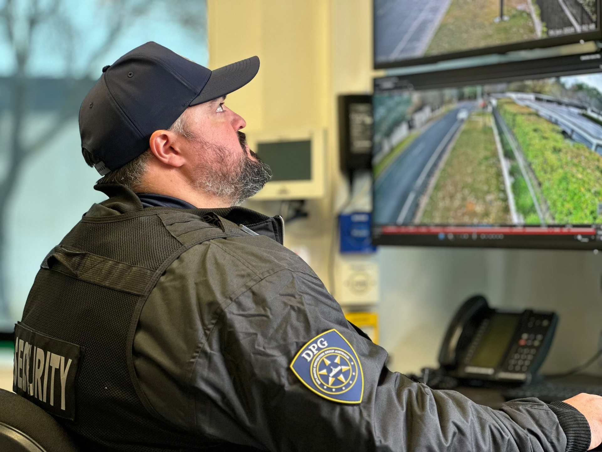 Security officer watching surveillance monitors. Wearing a cap and vest with 
