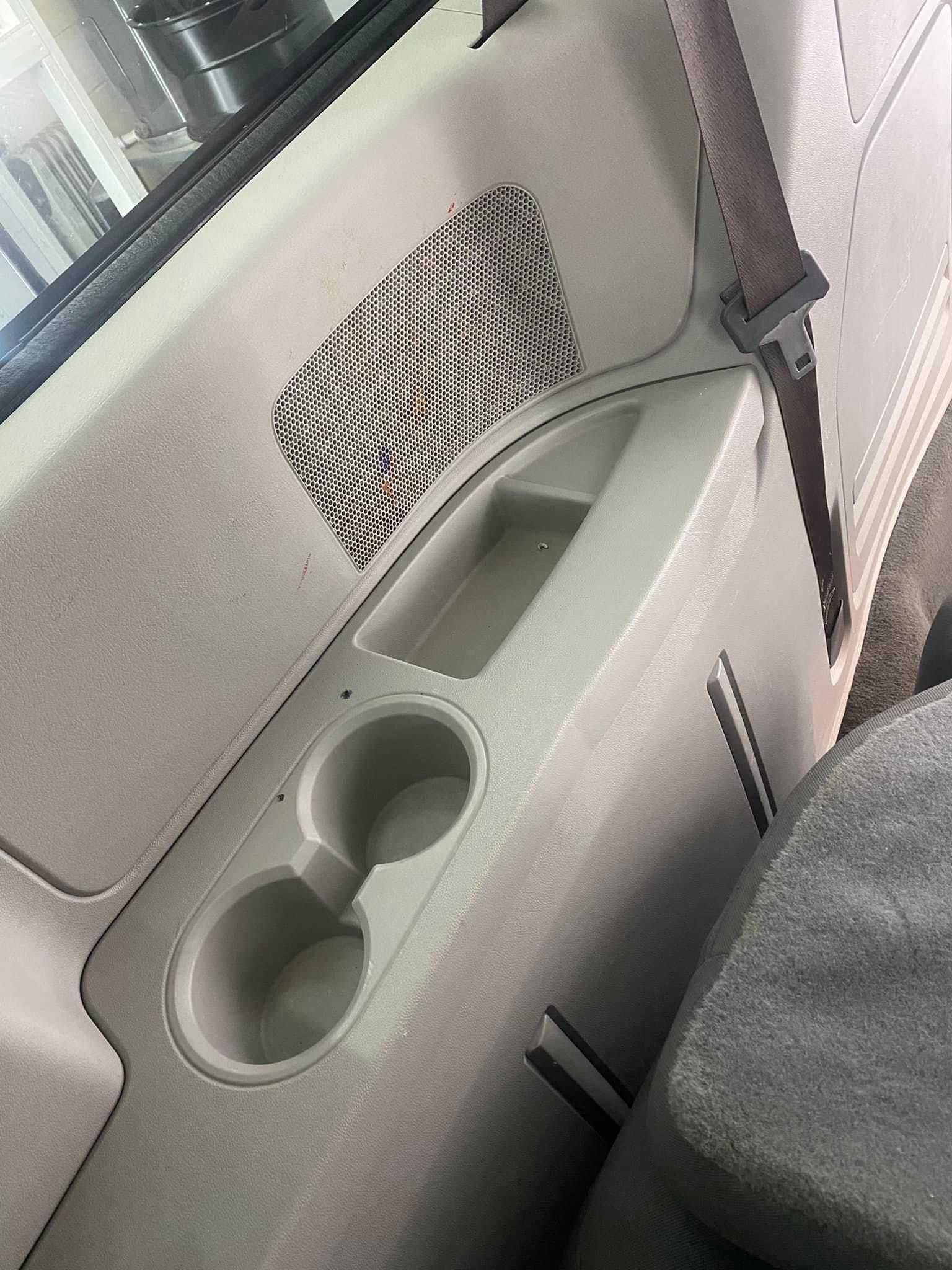 Car door with two cup holders, storage pocket, and seat belt buckle in a gray interior