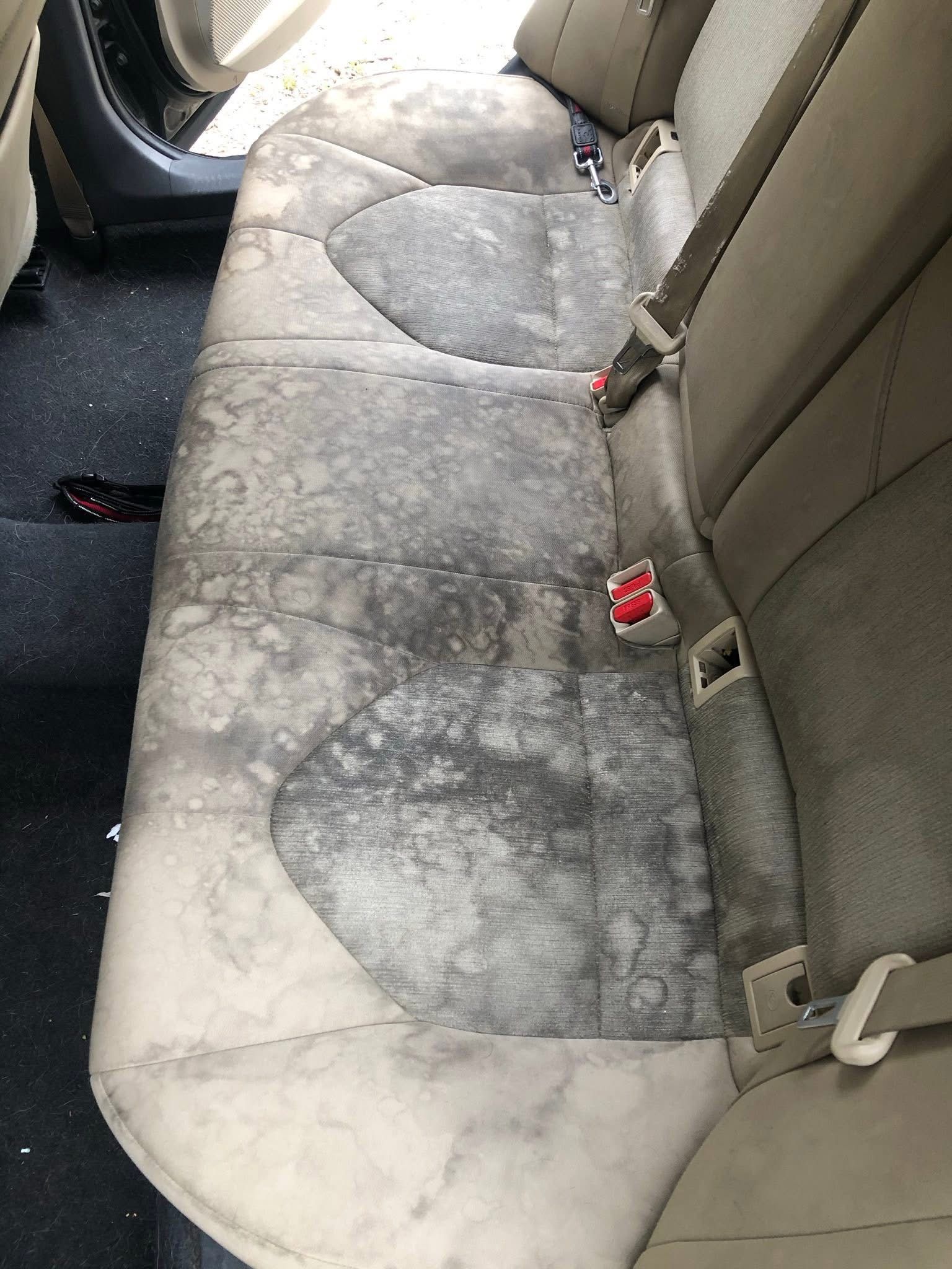 Dirty, stained rear car seat upholstery with worn gray and white cushions