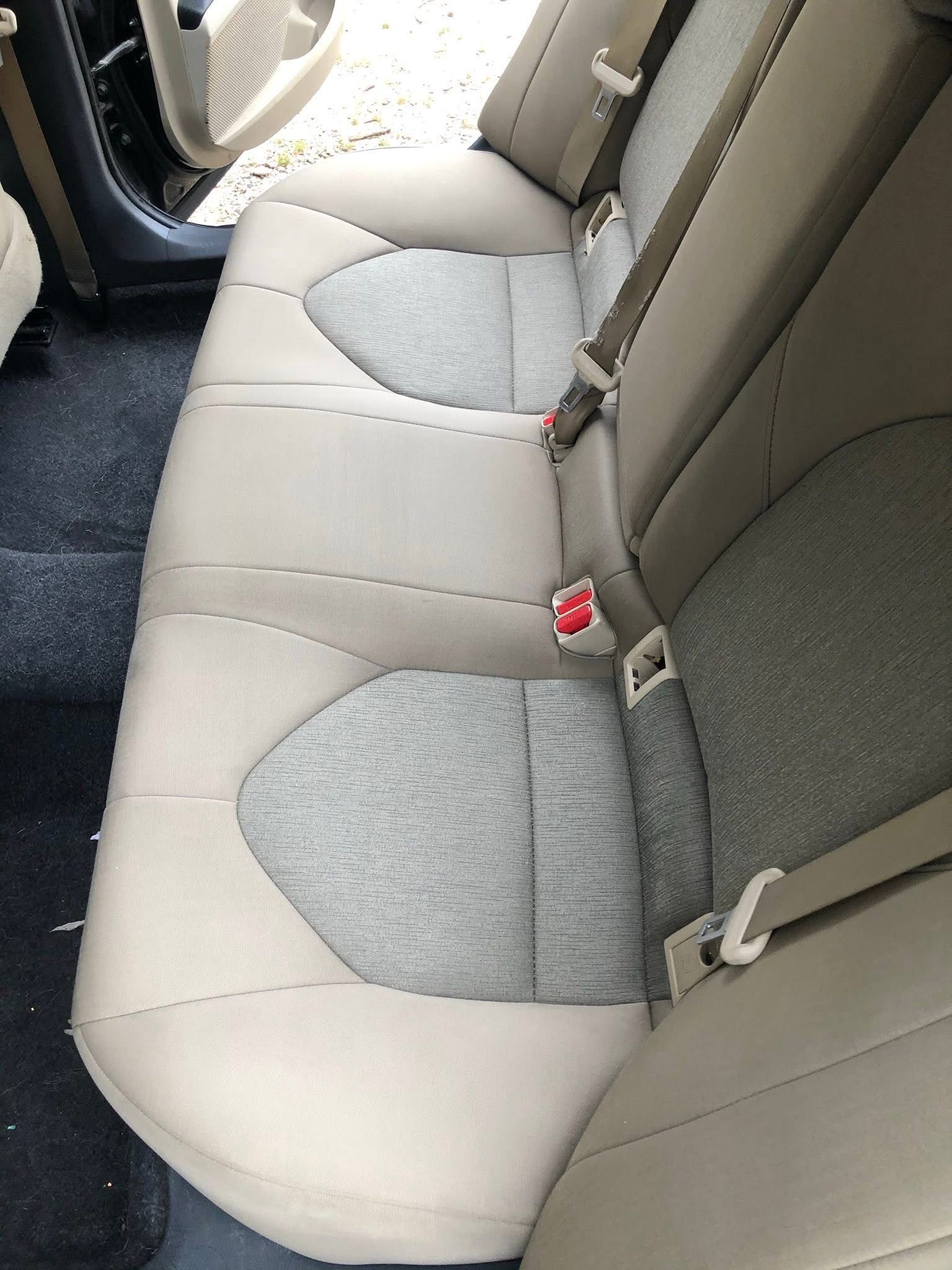 Back seat of a car with beige and gray upholstery and red seat belt buckles
