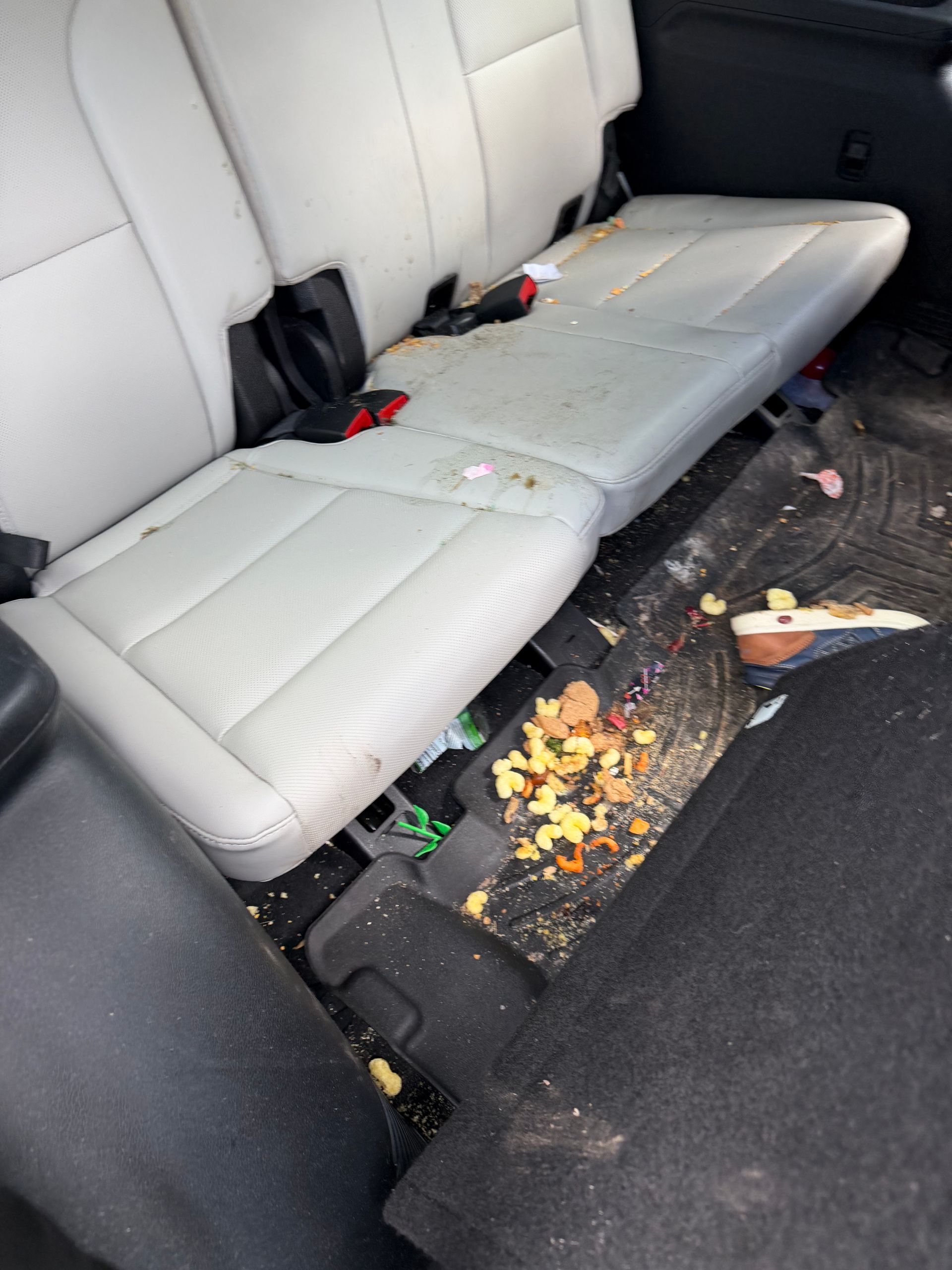 Back seat of a car with spilled food and crumbs on the floor and seat