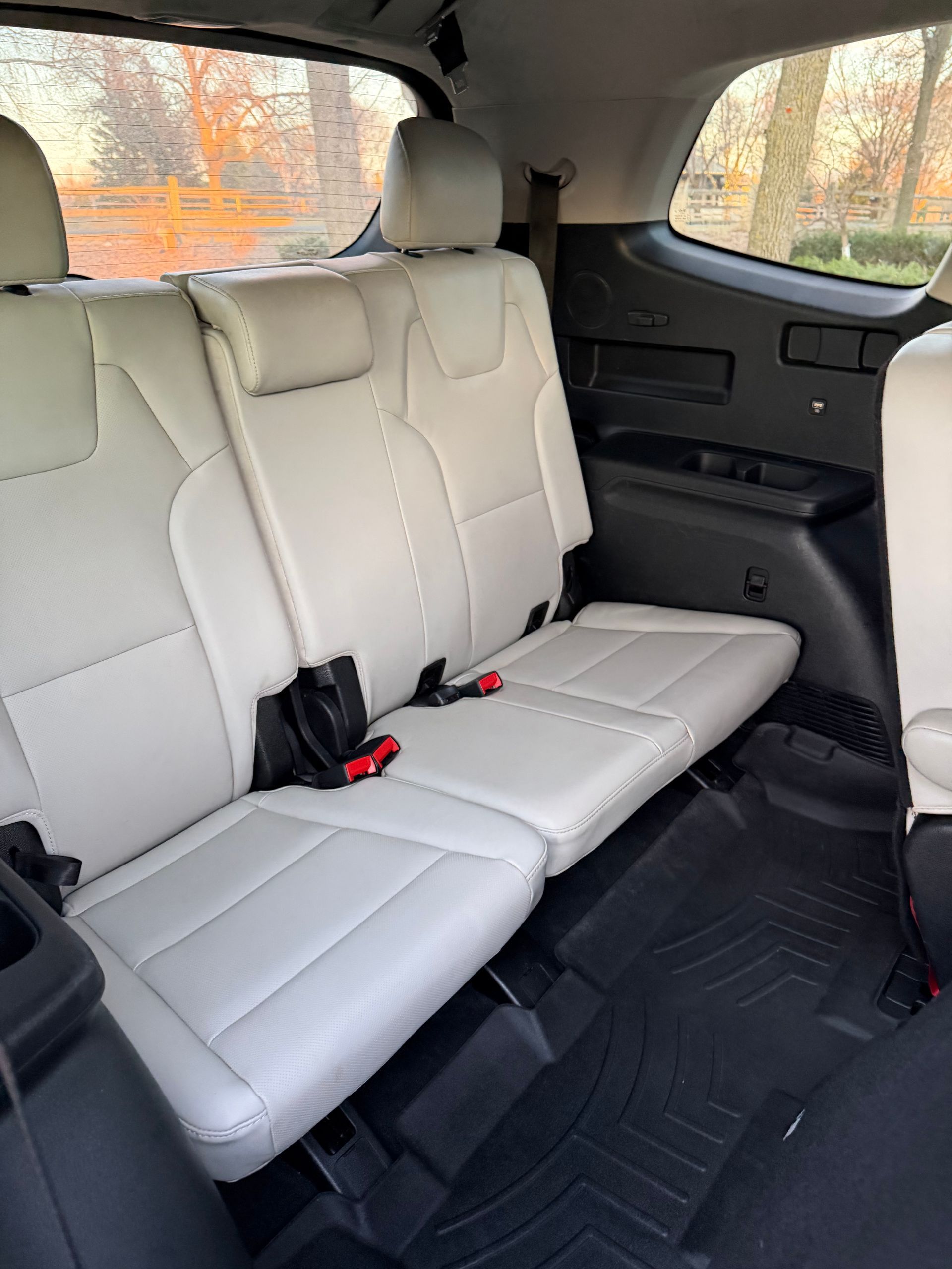 White leather SUV back seats with black floor mats and a rear side window view of autumn trees